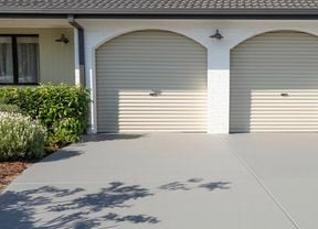 A freshly painted gray concrete driveway in front of a house with two garage doors.