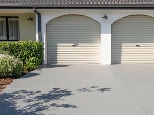 A freshly painted gray concrete driveway in front of a house with two garage doors.