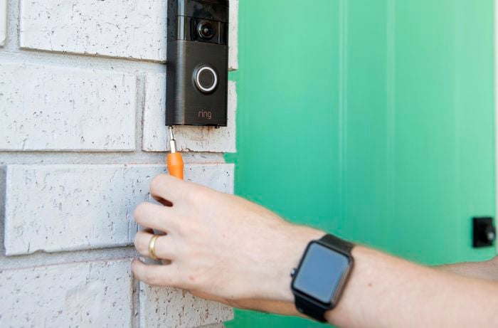 Person screwing doorbell back together after it has been wall-mounted.