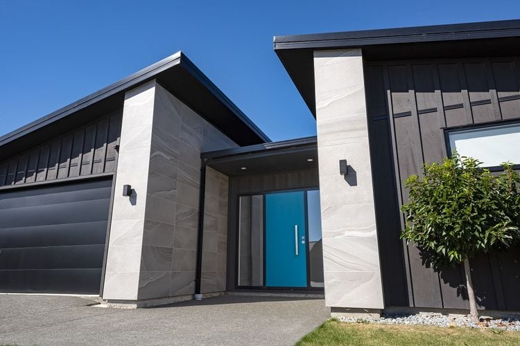 Exterior of a modern house with light and dark grey cladding and a blue front door