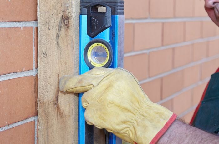 A person checking a timber post using a spirit level