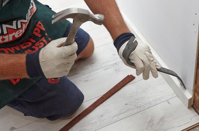 Person using hammer and pinch bar to remove skirting board.