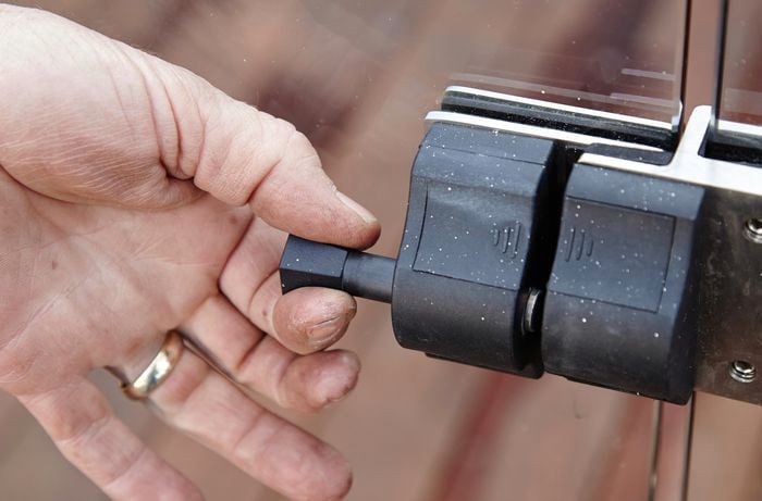 The latch of a glass pool fence being tested by a hand with a gold wedding band