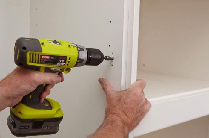 A hole being drilled into the side of a kitchen pantry wall