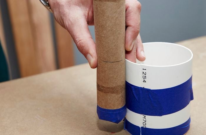 A person measuring a paper towel roll against a length of PVC pipe