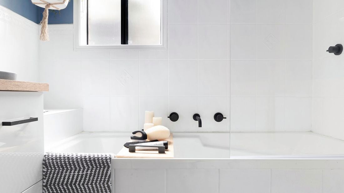 White bath in a bathroom with a towel draped over the side.