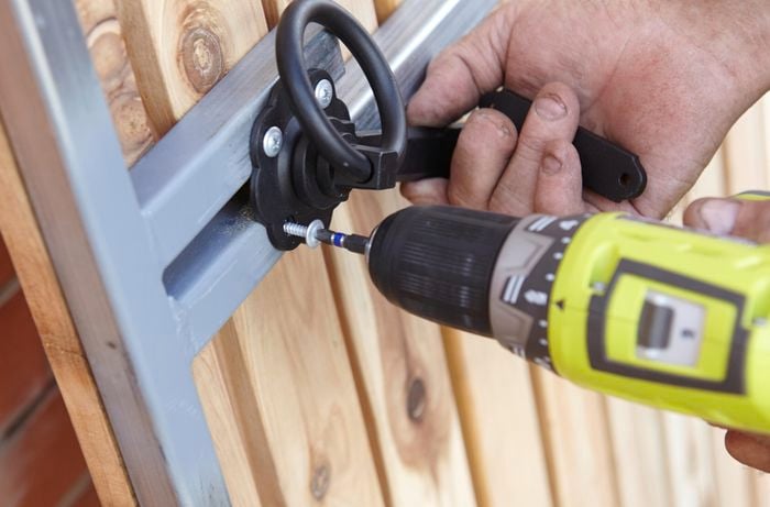 Person screwing a handle to a gate using a cordless driver