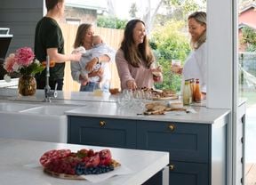 A group of people gathered around a kitchen chatting and laughing