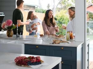 A group of people gathered around a kitchen chatting and laughing