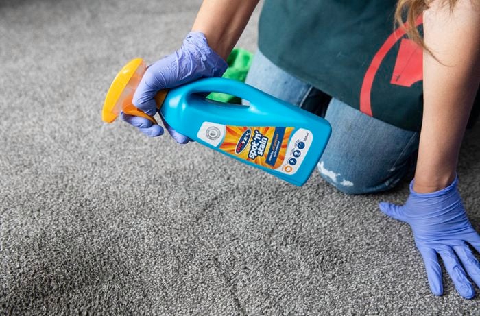 A person kneeling and spraying carpet with Bri-Tex Spot-n-Stain
