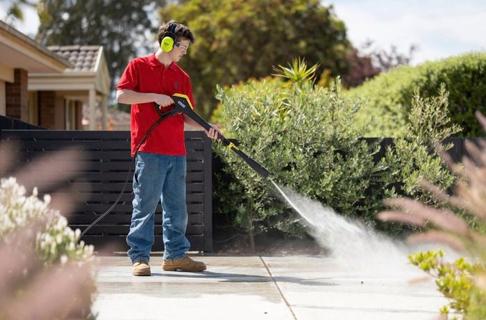 A Bunnings Team Member is using a pressure washer on the concrete surface to remove any dirt, dust, or loose material.