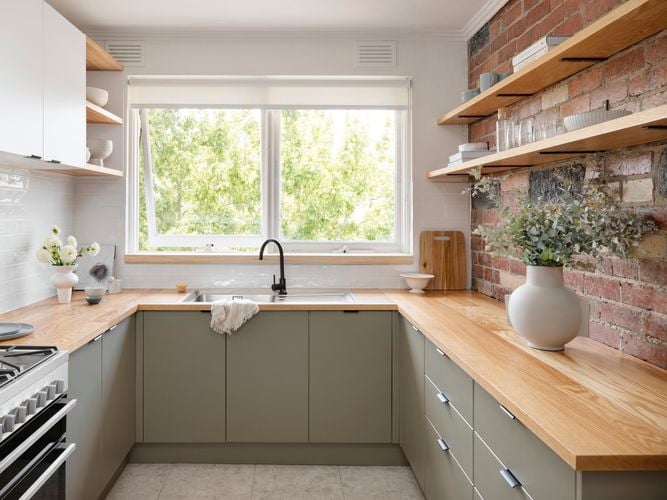 Cottage style kitchen with exposed brick wall, timber look benchtop and shelving.