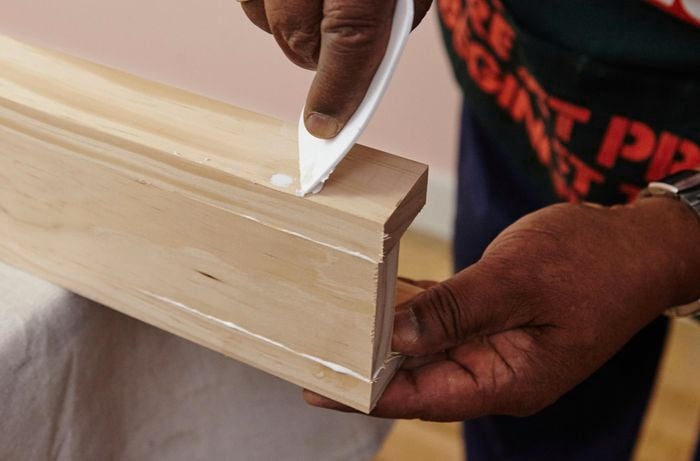 A person filling a hole in a length of pine timber with a plastic applicator