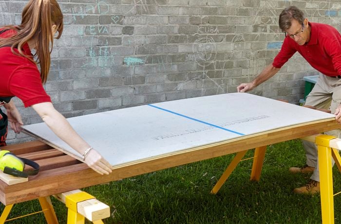 Two people attaching plywood to cement sheeting board.