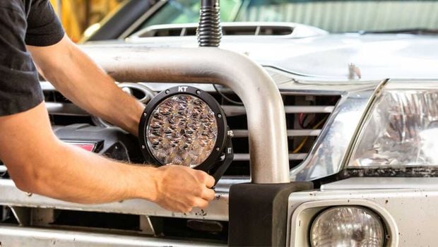 A person attaching a KT driving light to the bull bar of their car.