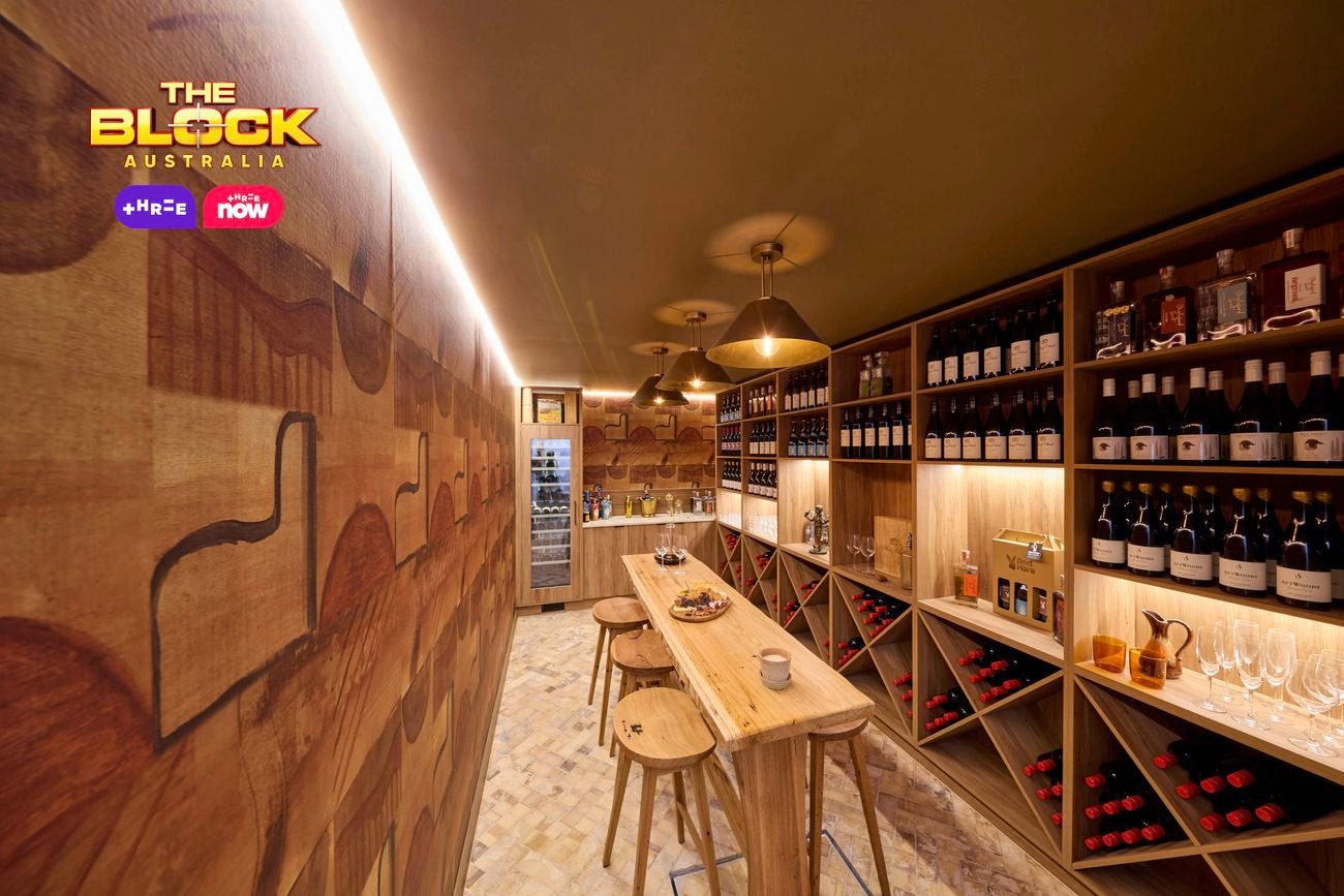 A bar area with lot of bottles of wine in it with a table and stools around it.