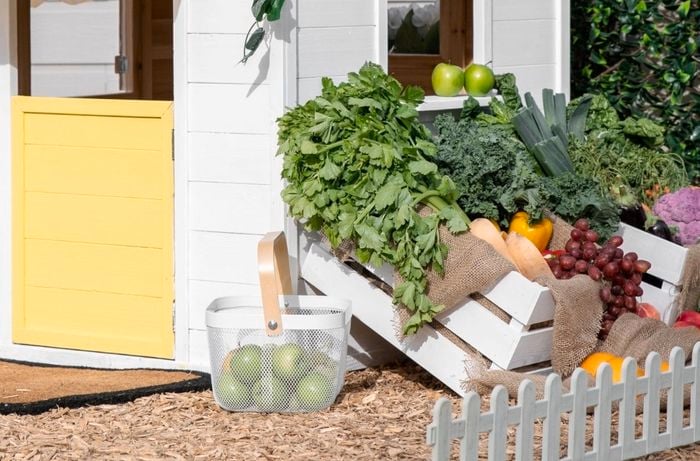 Various crates and baskets of fruit and vegetables displayed outside of a cubby house