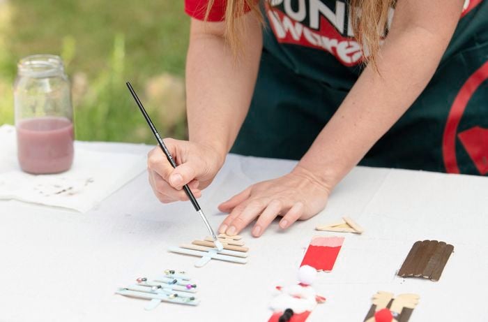 Using a paint brush to paint a popsicle stick Christmas tree decoration a shade of silver