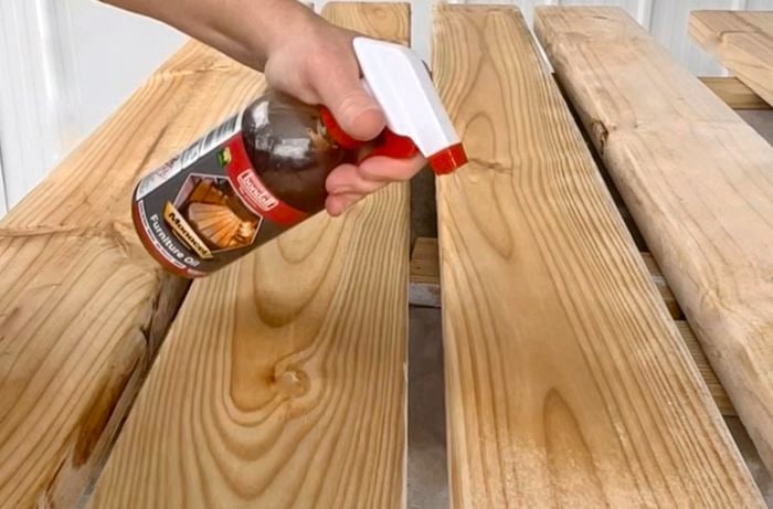 A person sprays furniture oil onto timber slats