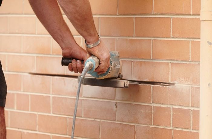 A person using an angle grinder to cut away mortar in a brick wall 
