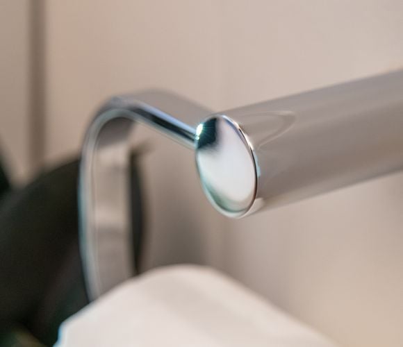 Close up of the fitting on a toilet paper holder. Chrome in colour and looks like a cylindrical shape with a C coming out of it.