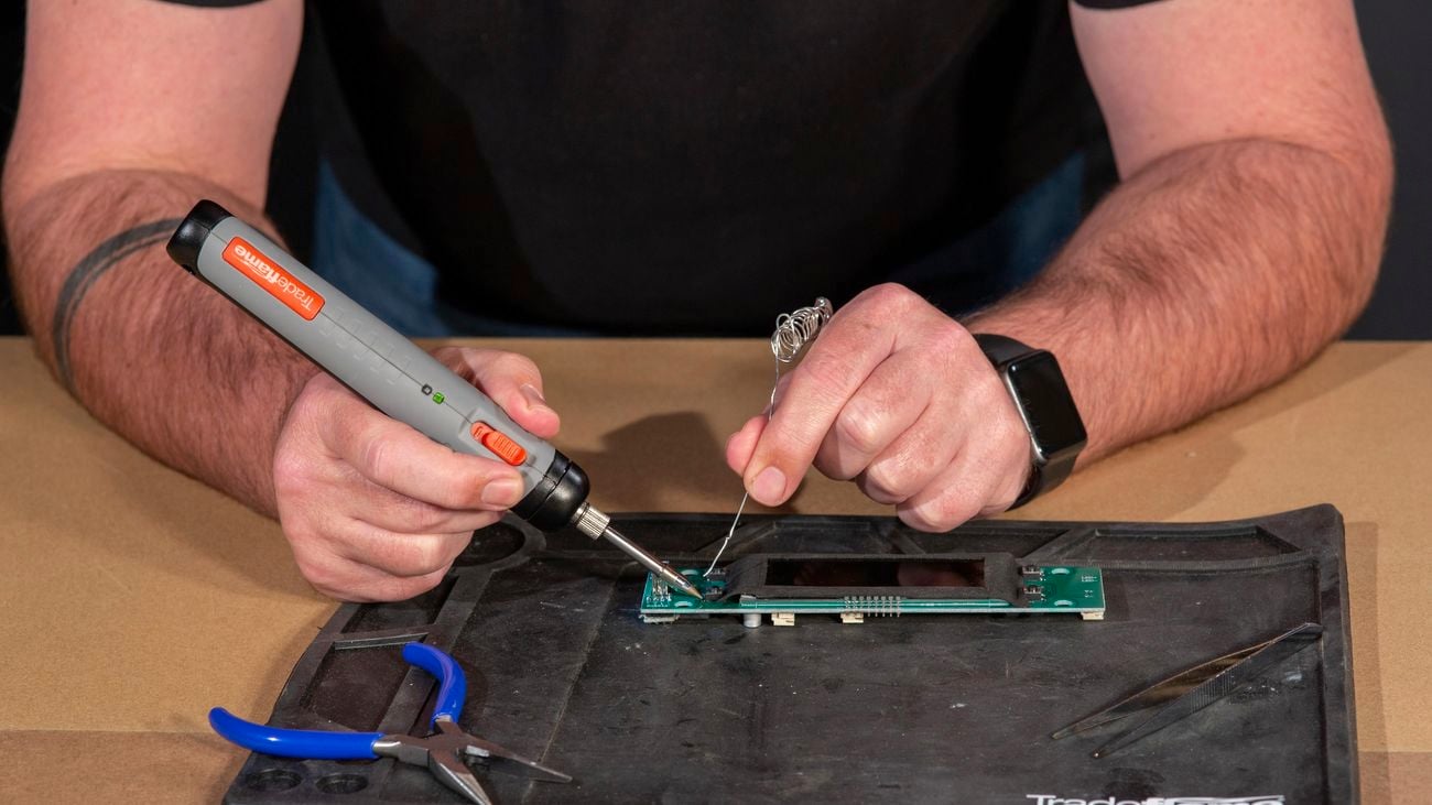 A man uses a soldering iron to melt metal alloy onto a circuit board. 