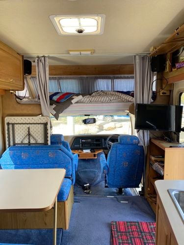 The interior of an old RV caravan with timber cabinetry and a blue couch.