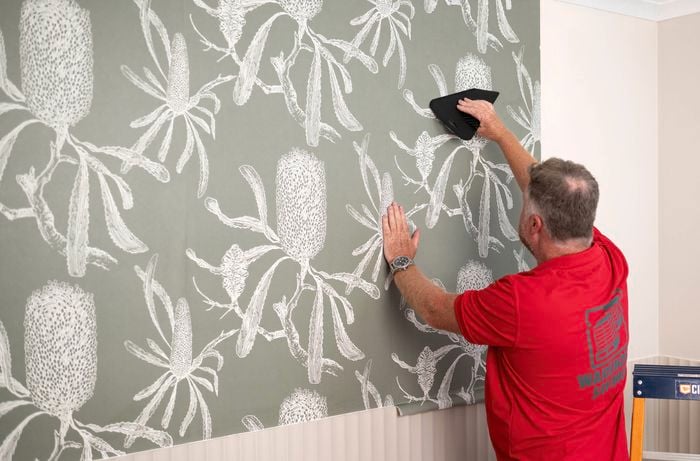 A Bunnings team member is using a wallpaper smoother to smooth out wallpaper placed on the wall.