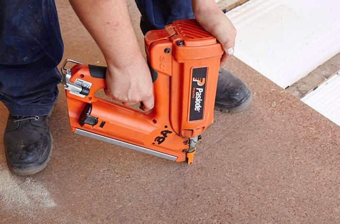A nail gun being used to secure chipboard to floor beams