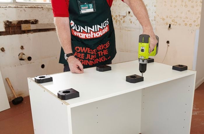 Person using a cordless driver to attach feet to a cabinet