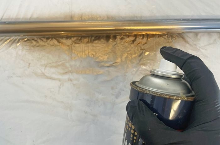 Close up image of a black gloved hand spraying gold paint on a metal rod to make a gallery wall
