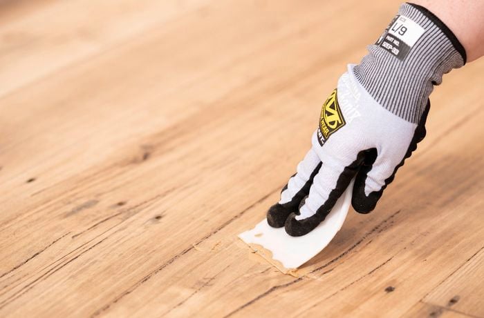 A person is using a scraper to apply wood filler into small gaps and imperfections in timber flooring after sanding. ​