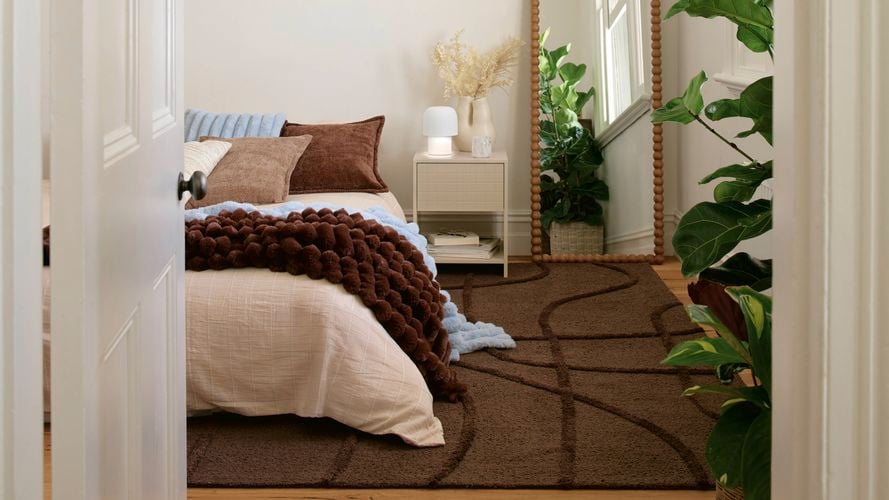 Bedroom interior with a neatly made bed, floor mirror, and indoor plants