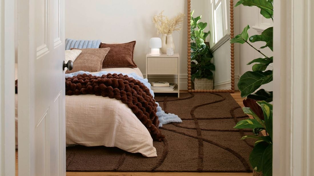 Bedroom interior with a neatly made bed, floor mirror, and indoor plants