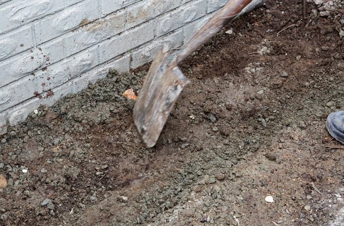 A person leveling the ground next to a house wall using a spade