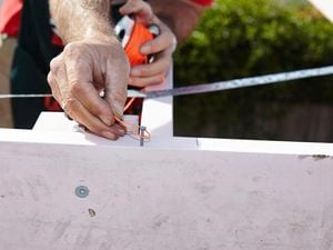 Person tying string around a nail on a timber beam