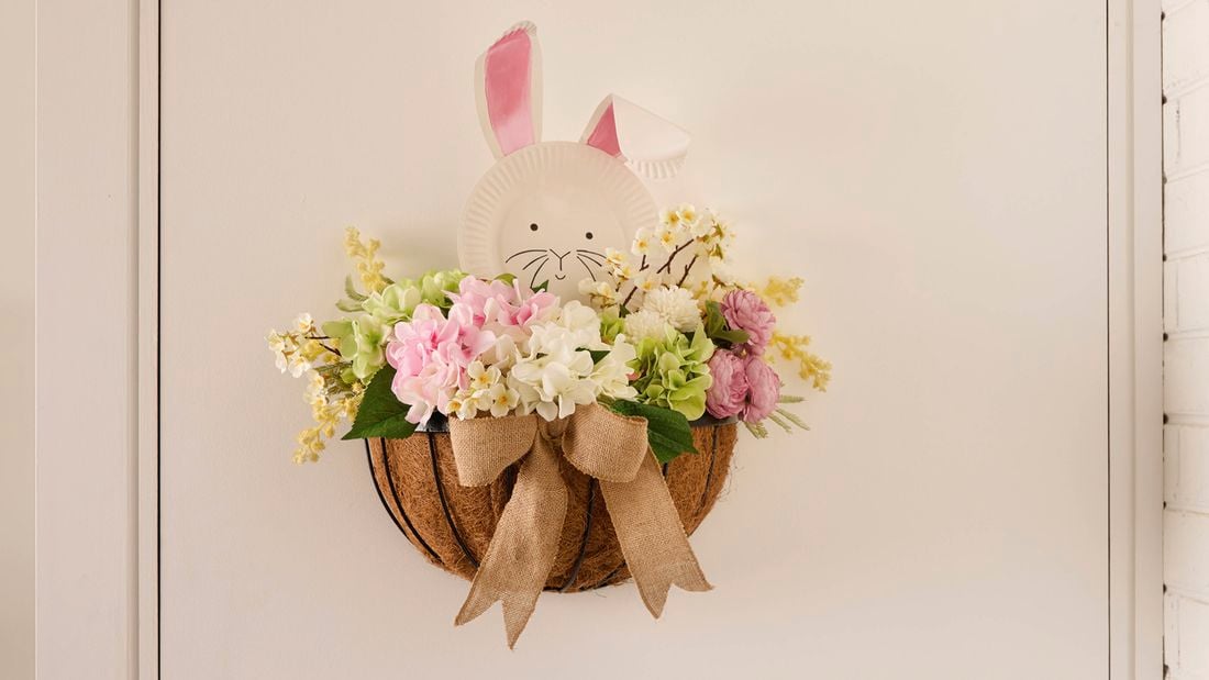 Hanging coir-lined wall basket with pastel flowers and a bow, a paper plate bunny face with pink ears peeking over the top