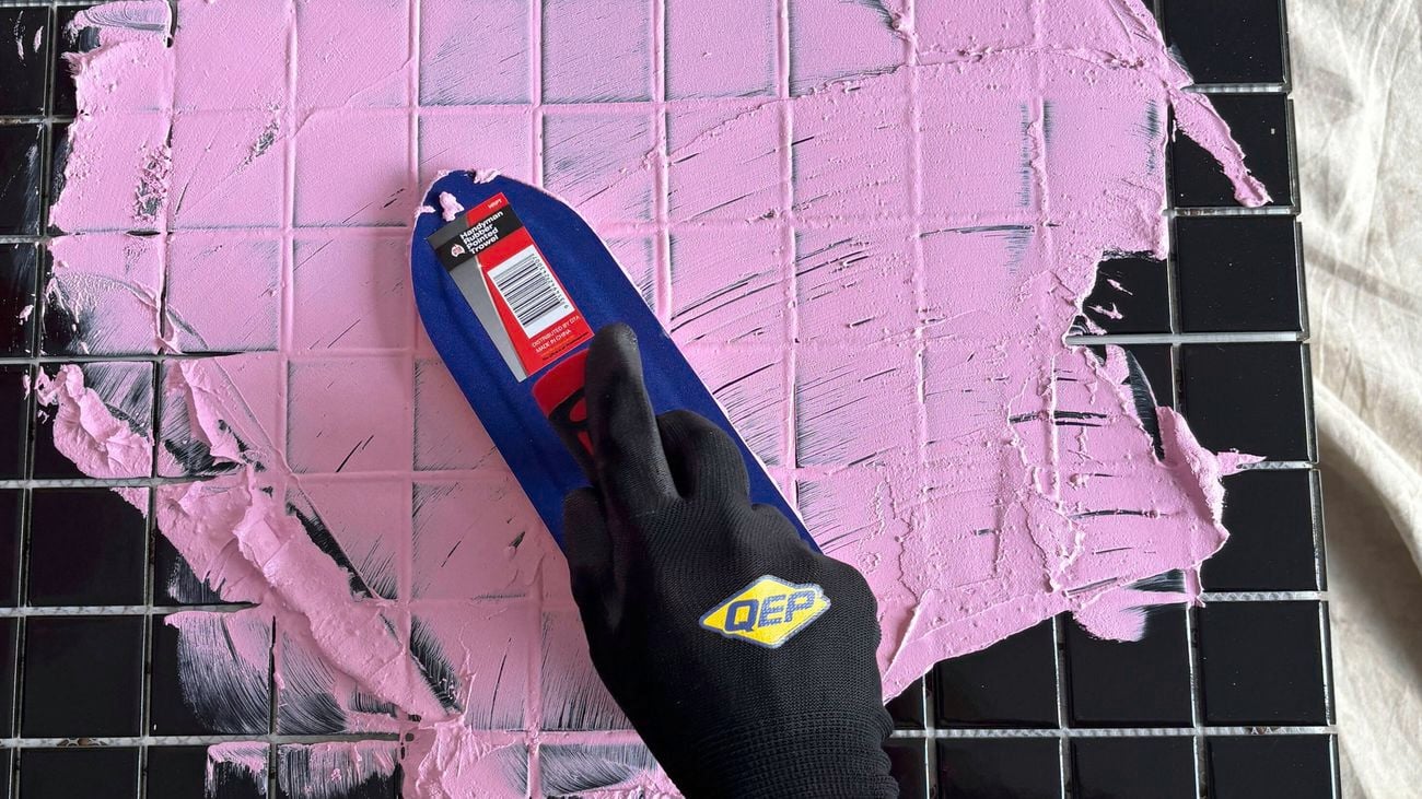 a gloved hand grouting black tiles.
