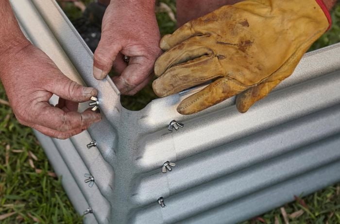 Person tightening nuts and bolts to hold corrugated iron garden bed together.