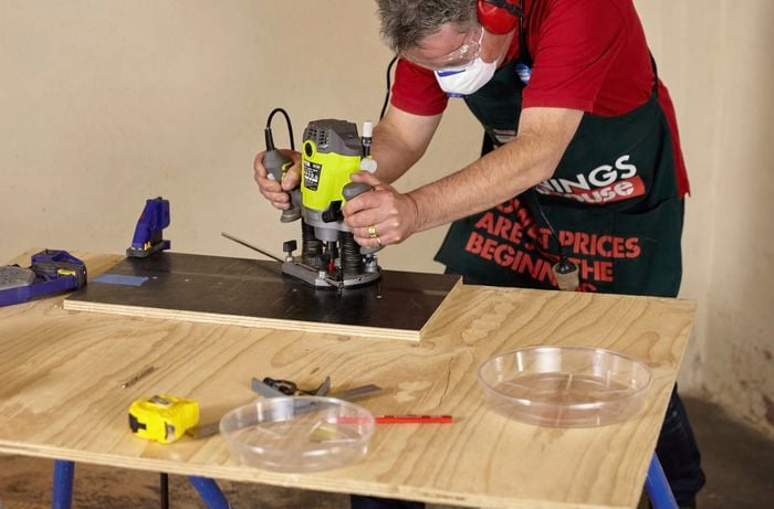 A person using a router to cut a circular hole in a piece of plywood