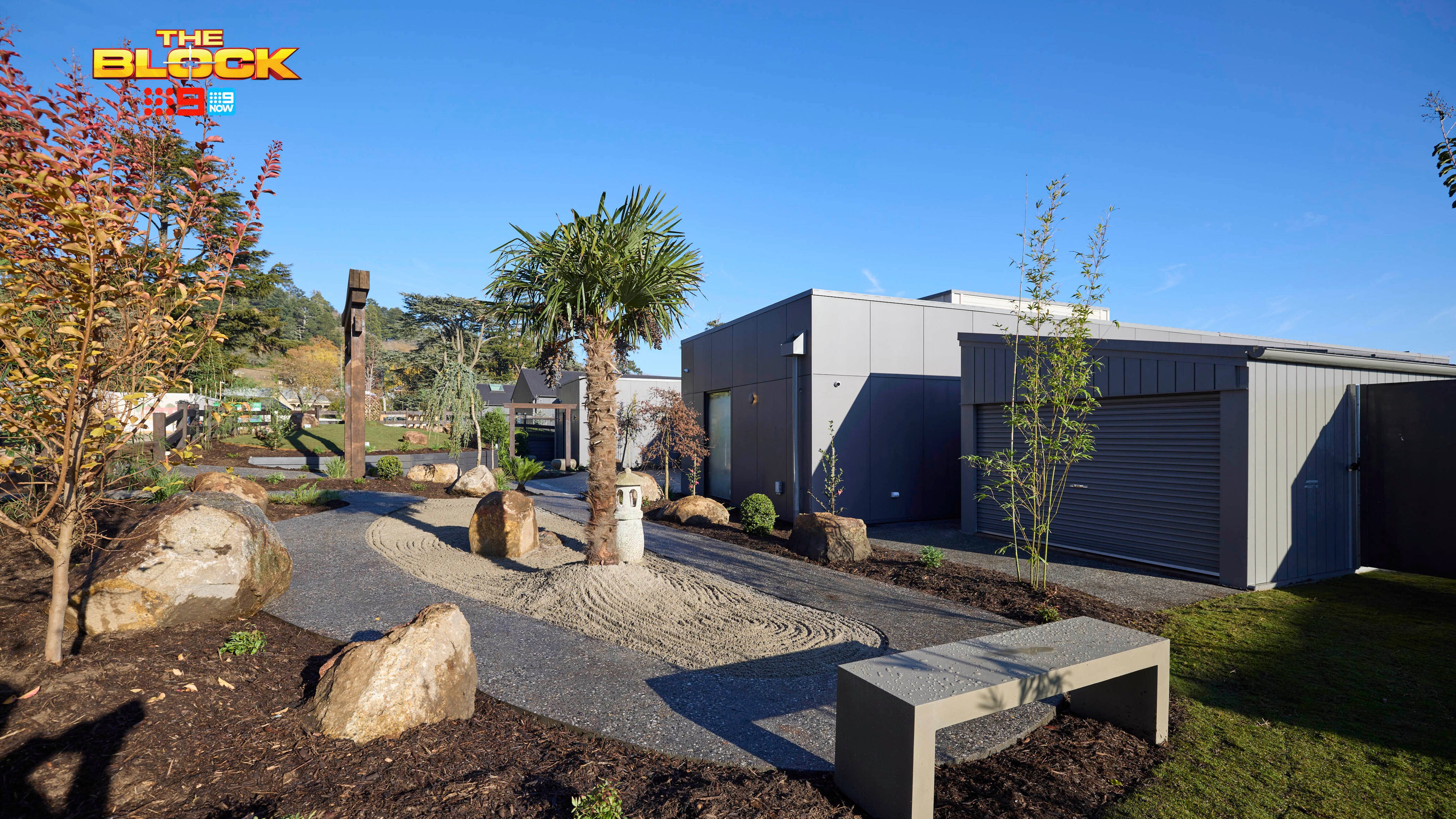 The front area of a house with a bench seat, rocks, grassed area and trees in it.