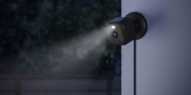 A black security camera with a light on it attached to an outside wall.