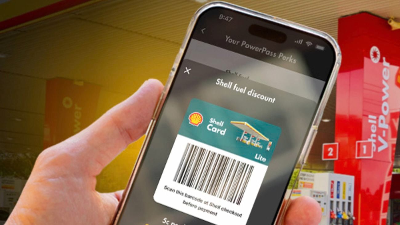 A hand holds a mobile phone showing a barcode for a Shell Card Lite fuel discount.