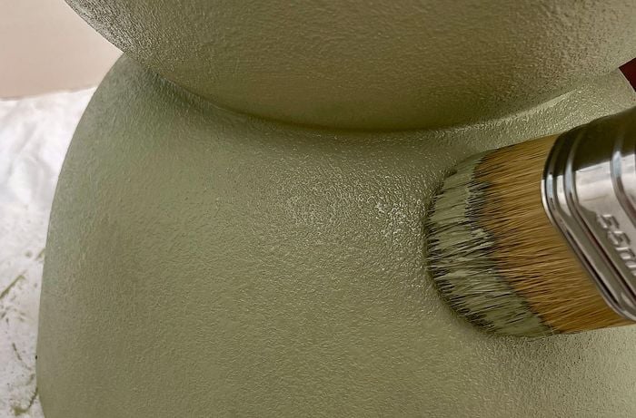 A person uses a chalk brush to create a textured surface on a planter pot