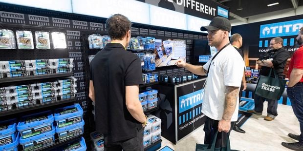 Two people browse Titan-branded hardware products at a trade show booth while speaking with a product expert.