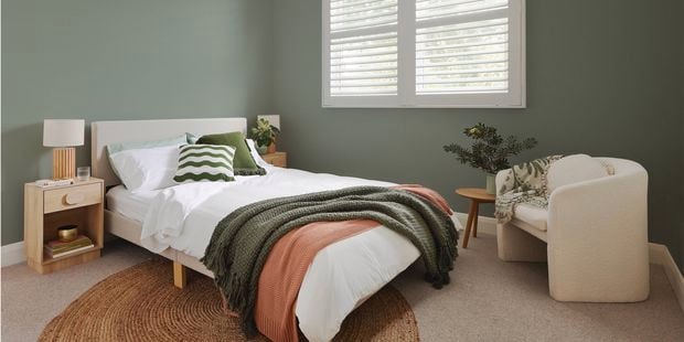A stylish bedroom showcasing green walls with a bed and armchair in the foreground.