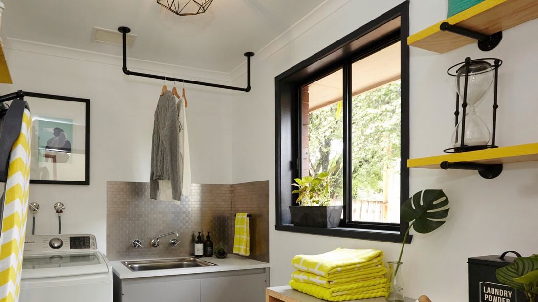 A renovated laundry with towels, a ironing board, hanging clothes and a washing machine.