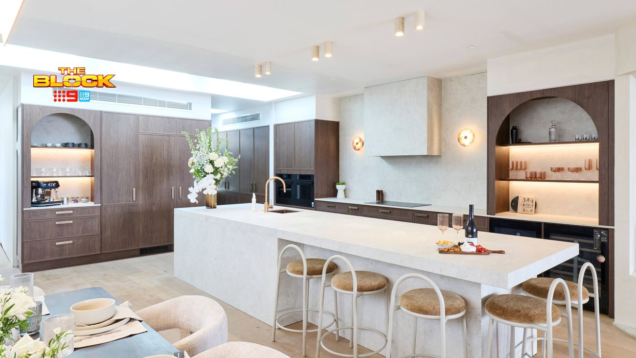 Contemporary kitchen featuring a large stone island bench, dark timber cabinetry, arched display shelving and bar stools.