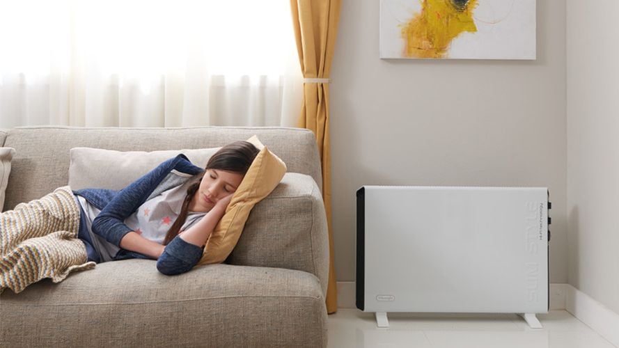 A young woman lying on a couch in front of an indoor heater