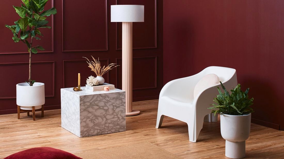 A lounge room with a chair, pot plants, lamp and table in it.